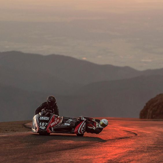 racing motorcycle sidecar racing on the Pikes Peak mountain in sunrise, and the passenger hangs off the side almost dragging his shoulder