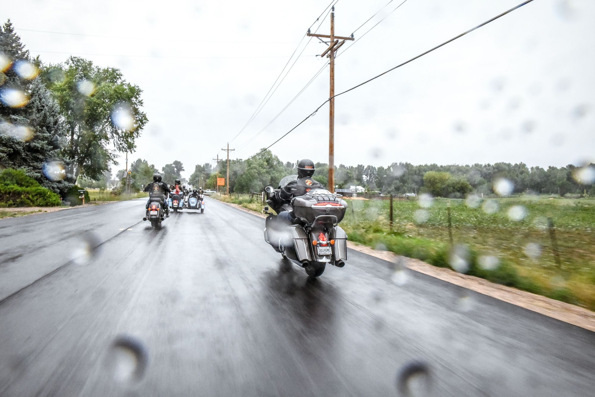 Motorcycle riders and sidecar riding in the rain on a highway road.