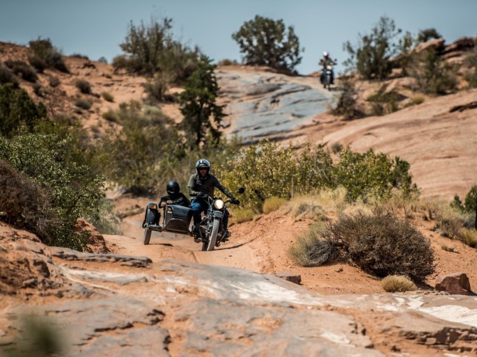 Motorcycle sidecar Ural rides off road in Moab Utah with motorcycle in background on trail.
