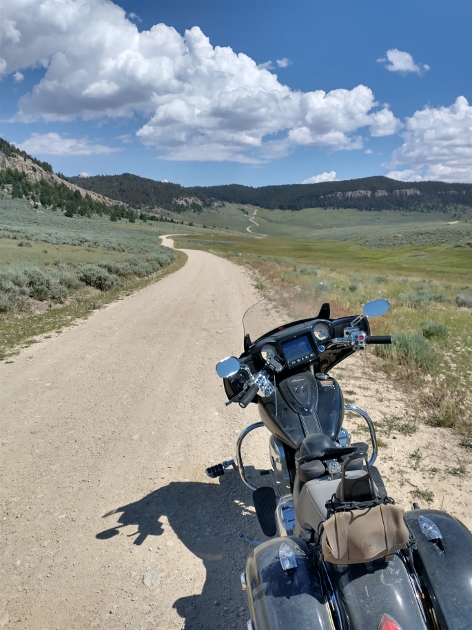 motorcycle on dirt gravel road in wyoming mountain forest, sky, clouds