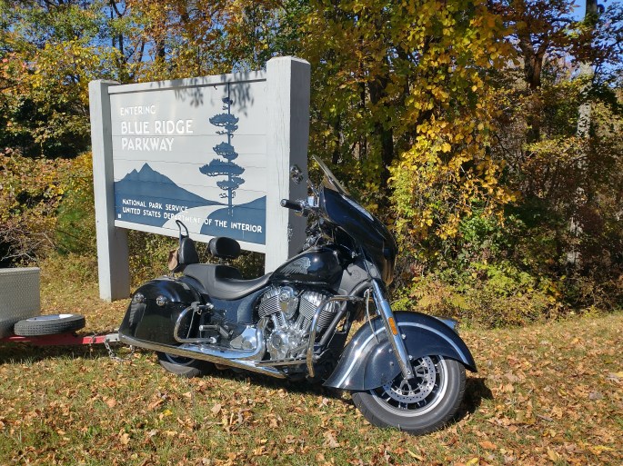 indian chieftain motorcycle in forest with autumn leaves and blue ridge parkway sign, trees, trailer.