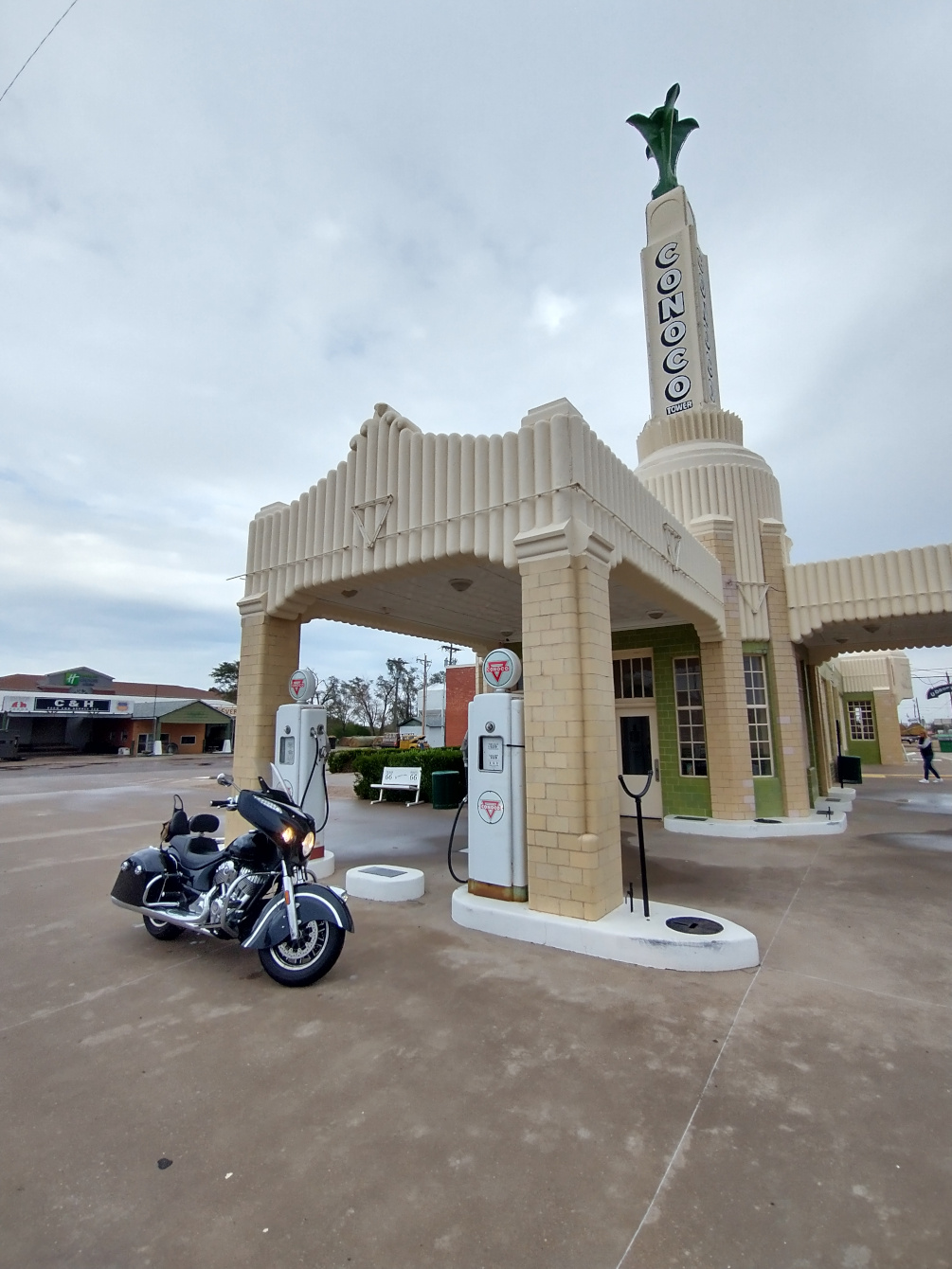 a restored Conoco filling station with a mix of styling from the 1930's and 1950's. Well preserved fuel pumps sit at attention while a modern but classically styled Indian Chieftain motorcycle parks in front of them.