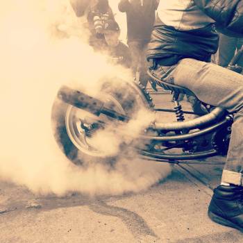 sepia image custom motorcycle doing burnout in parking lot with tire smoke