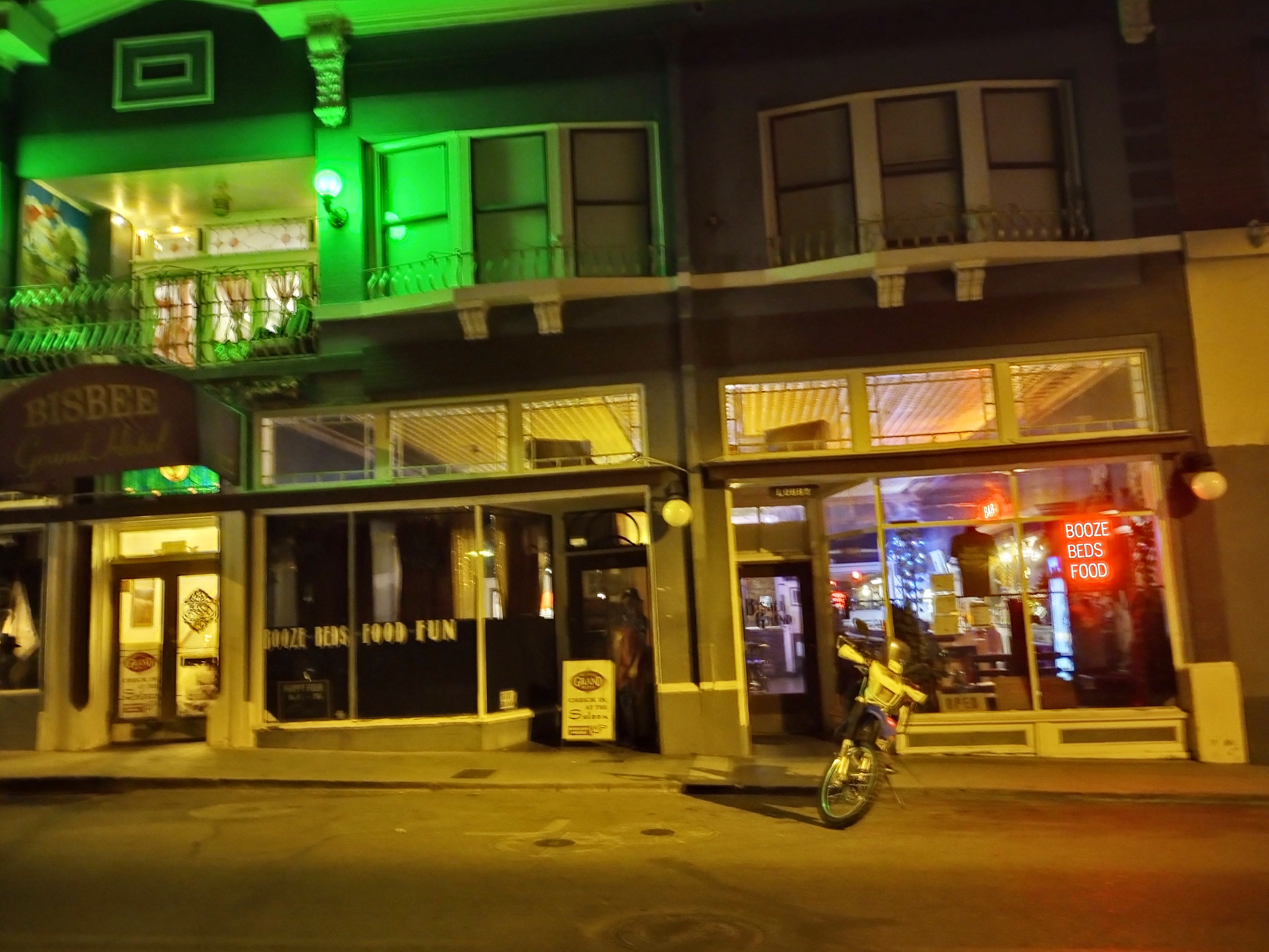 motorcycle dirt bike parked at night on street in bisbee arizona in front of the grand hotel, with neon lights in windows and a quiet feel