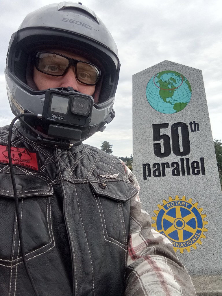 person standing with motorcycle helmet next to 50th parallel stone marker