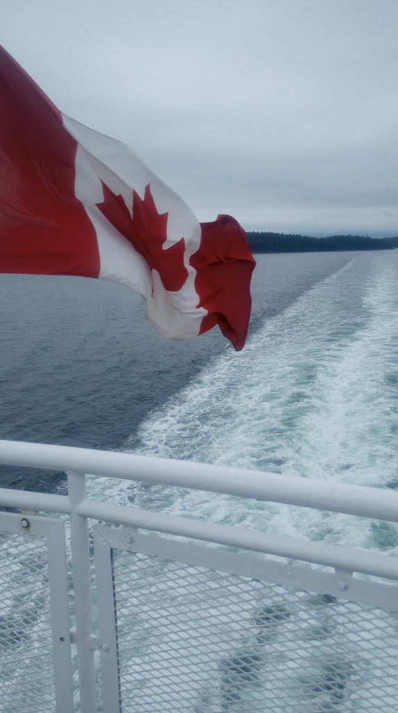 canadian flag waving off the fantail of a vehicle ferry with a large wake trailing behind