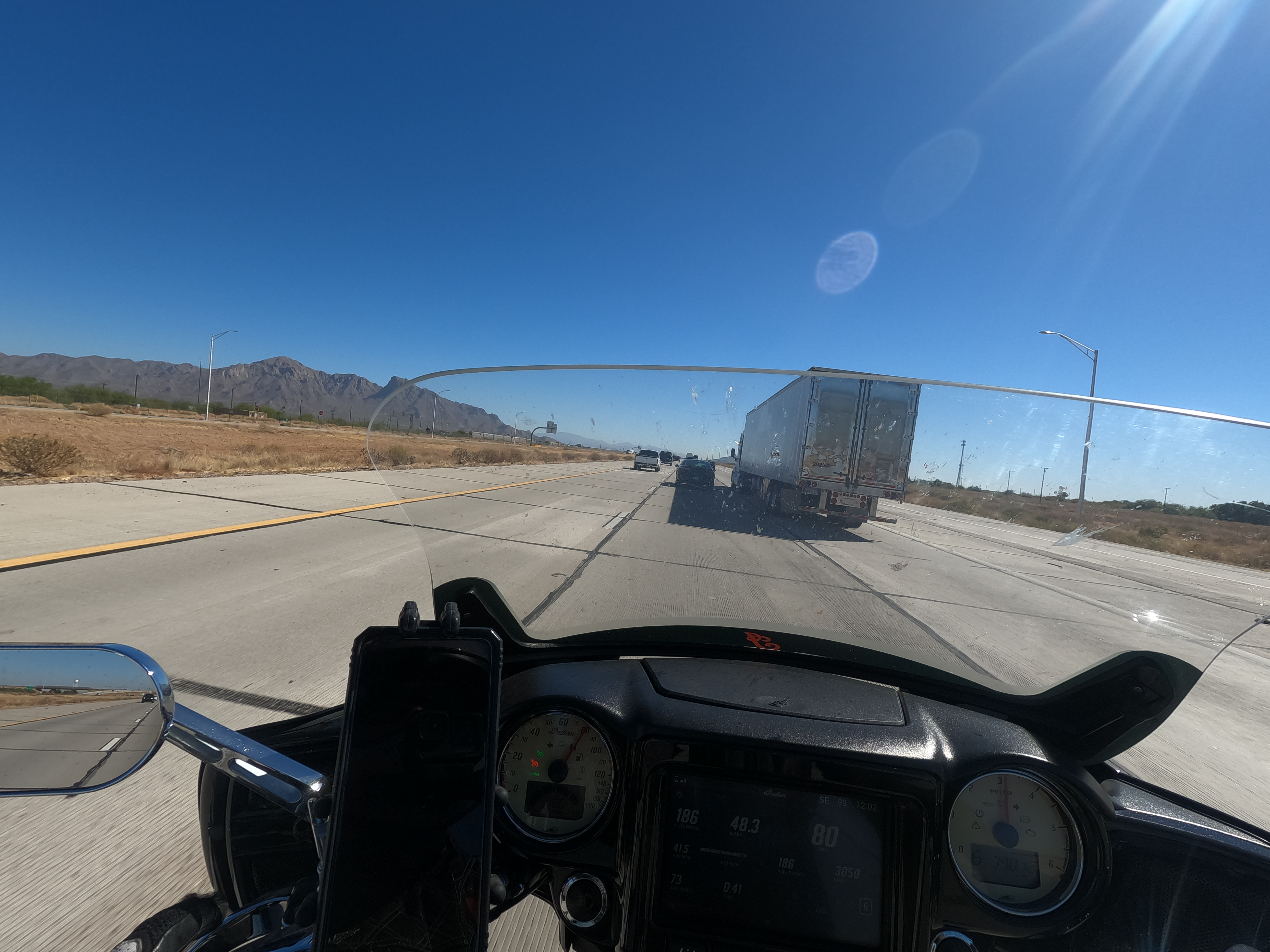 pov of dmotorcycle on interstate highway in the desert with tractor trailer and other cars ahead on a concrete roadway