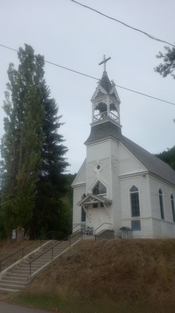 an old wooden church on a small hill, with bell tower and cross on top. Stairs lead up to the entrance