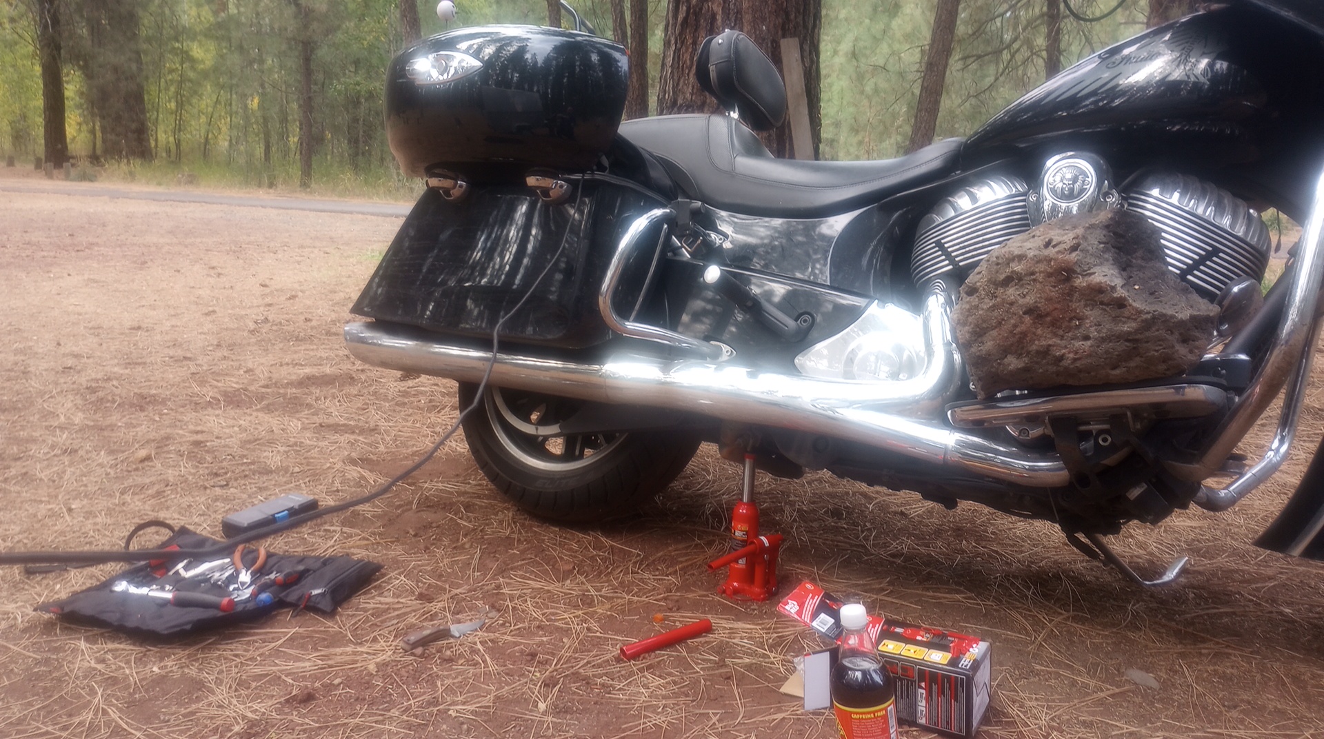 A motorcycle propped precariously on a bottle jack with a large stone on the footboards for balance the center of gravity
