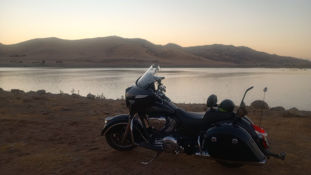 Indian CHieftain motorcycle parked in front of a reservoir with low hills covered in dry grass and sparse trees