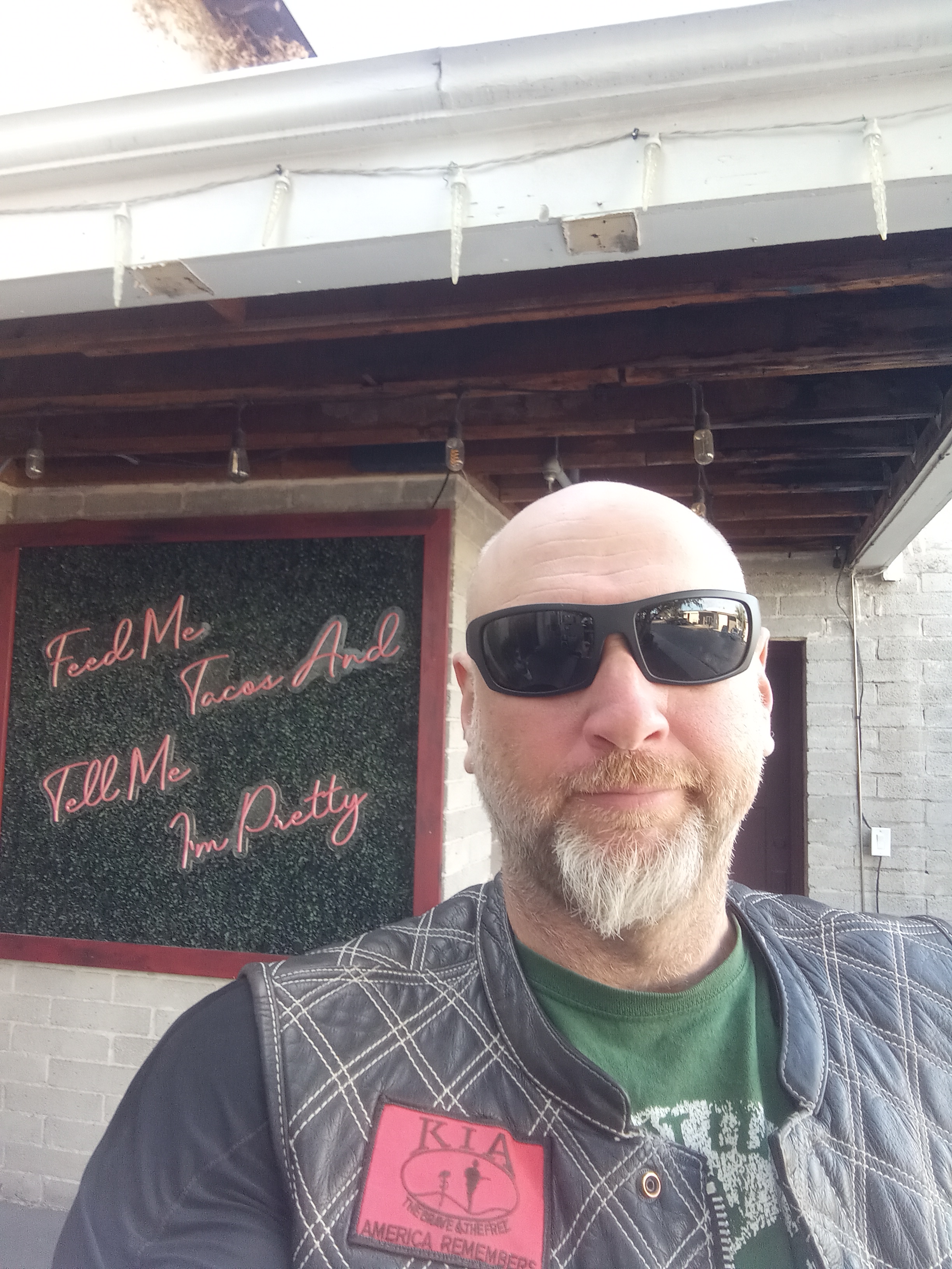 selfie of Johnny Killmore stadning infront of a sign saying "feed me tacos and tell me I'm pretty."