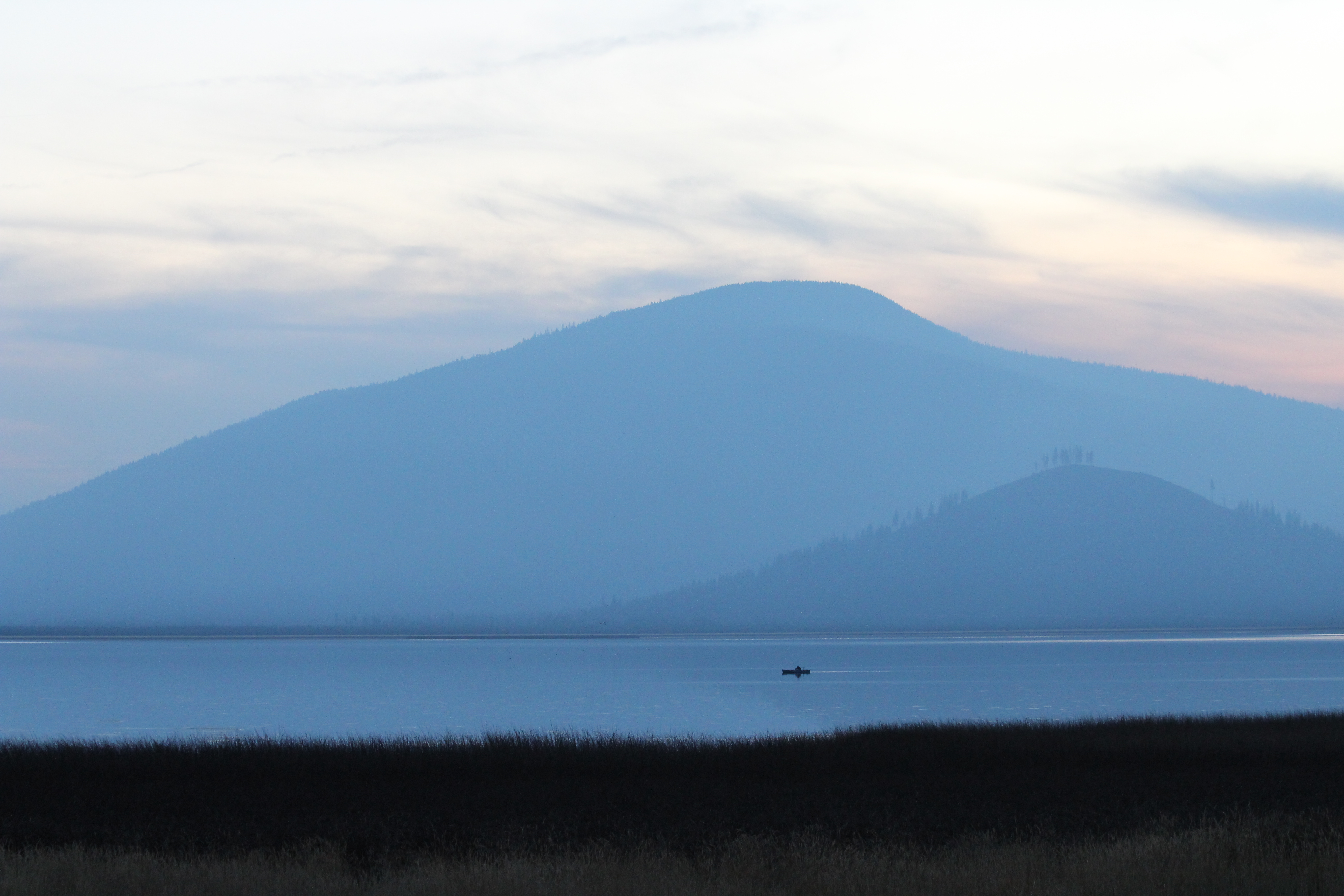 sunset over Davis Lake. The water is still and a single canoe glides across. The mountains are shadowing in a deep blue as the final sunlight behind it goes from orange to a blue-orange