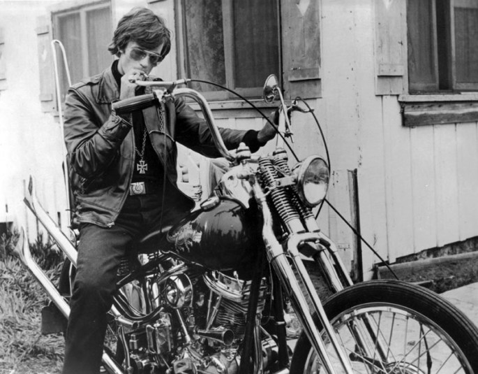 Black and white of Peter Fonda in character for The Wild Angels, sitting on his chopper smoking a joint