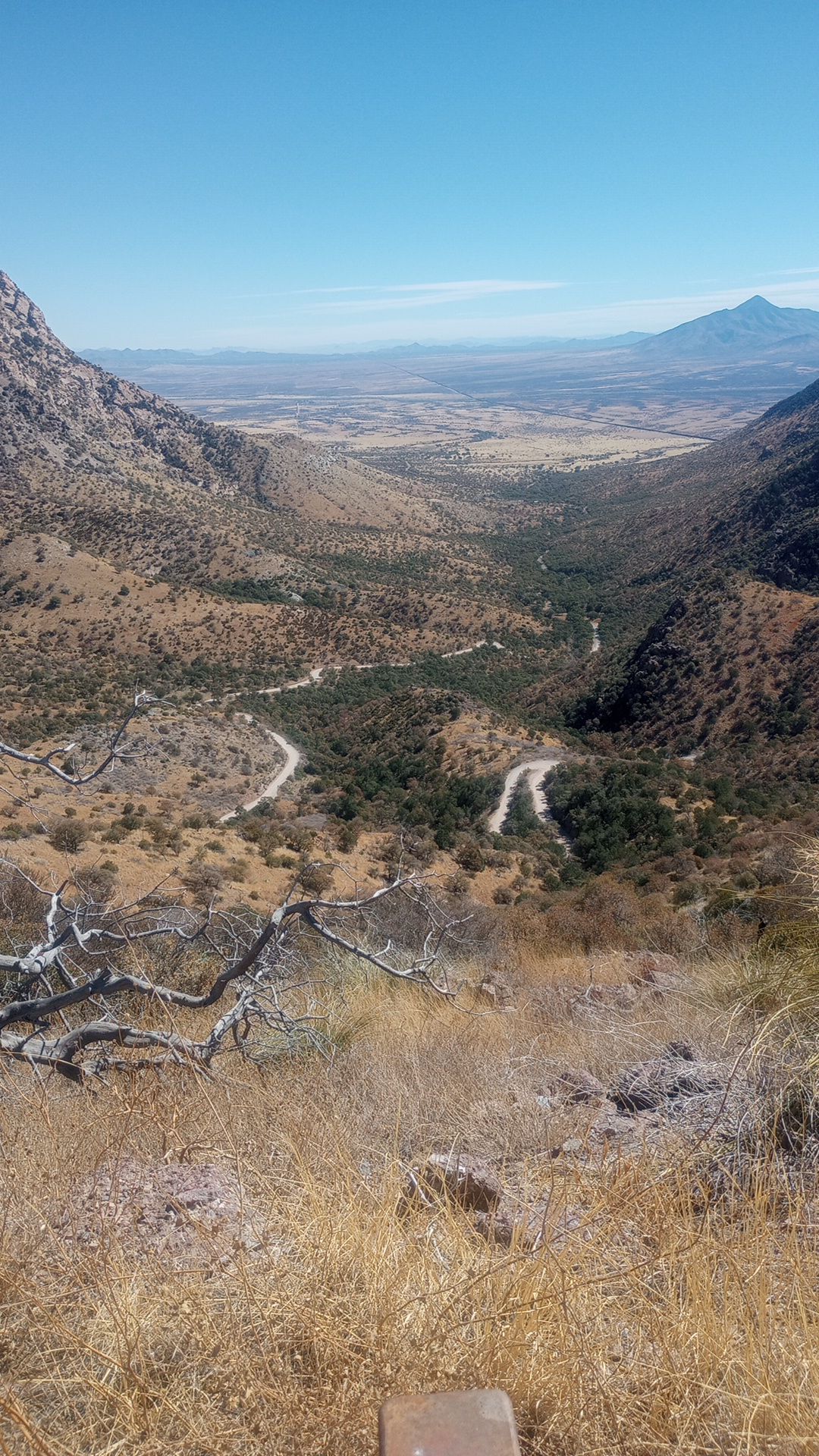 a desert mountain view looking down into a steep valley that has a winding dirt road snaking up it