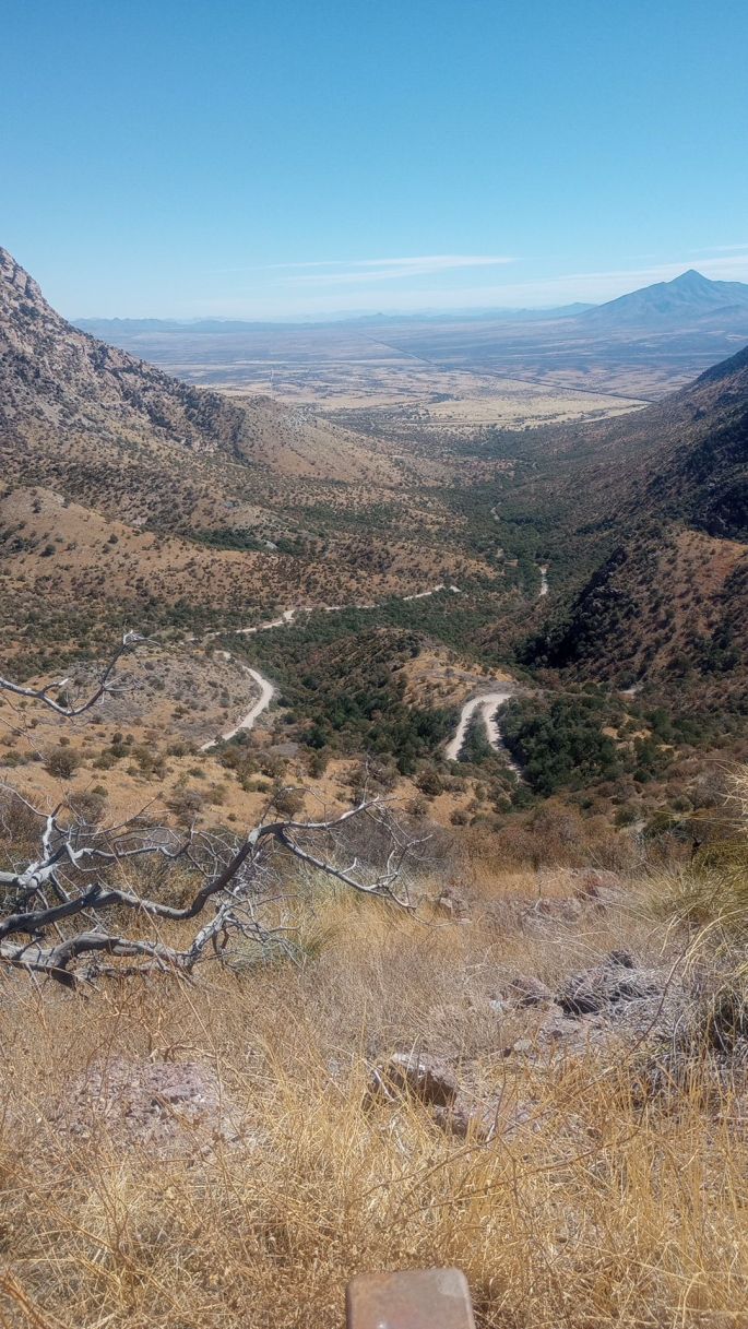 a desert mountain view looking down into a steep valley that has a winding dirt road snaking up it