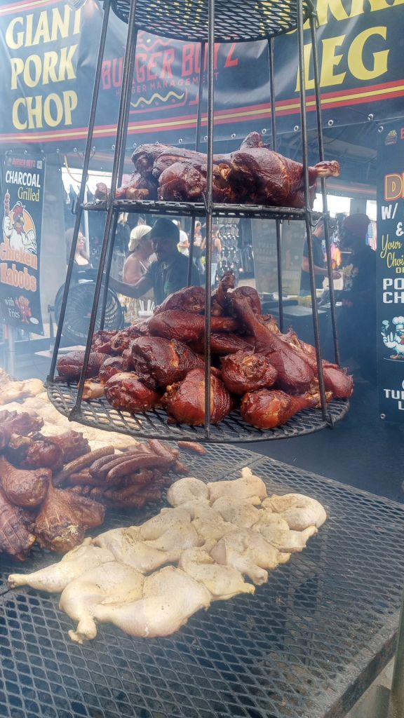 barbecue cooks on the grill while whole turkey legs hang above in racks