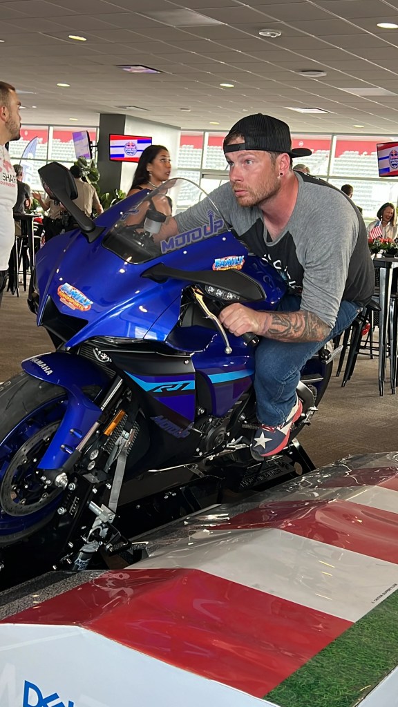 person poses on a sports motorcycle that is a static display, made to look like it is leaning through a corner on a race track