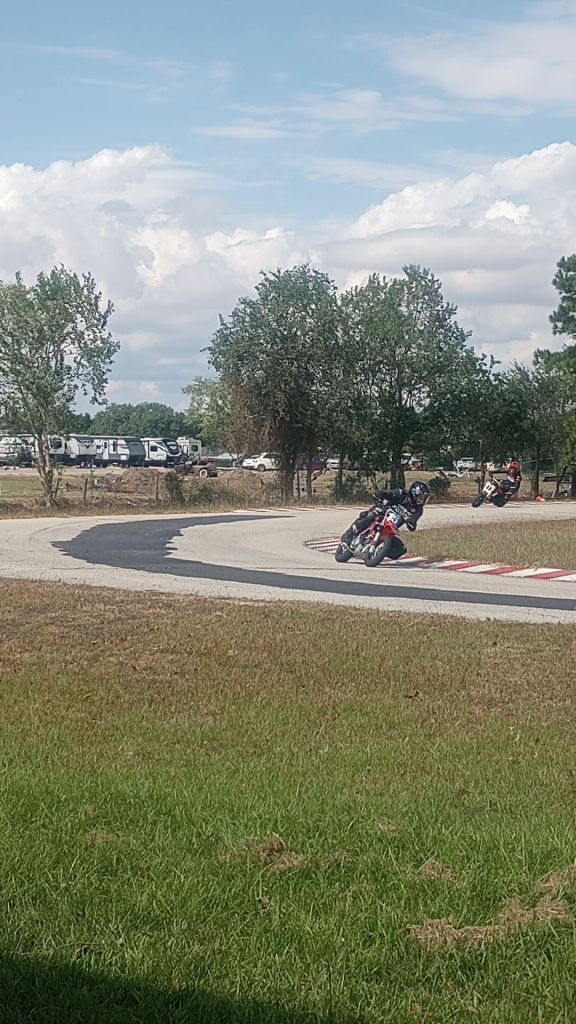 mini motorcycles circulate on a kart racing track with tall trees in the background